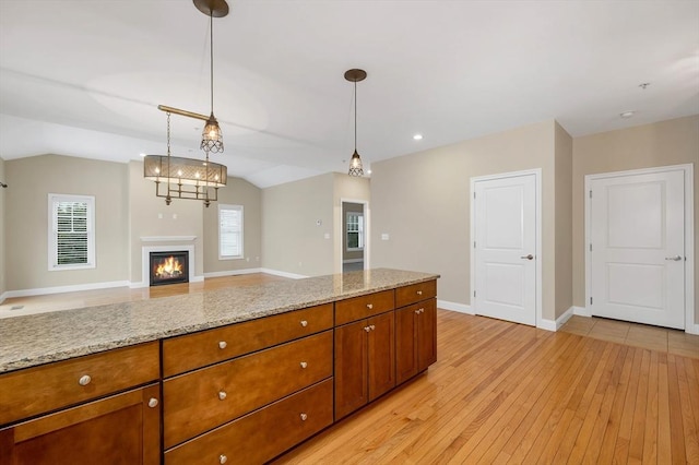 kitchen featuring light stone counters, lofted ceiling, hanging light fixtures, and light hardwood / wood-style flooring