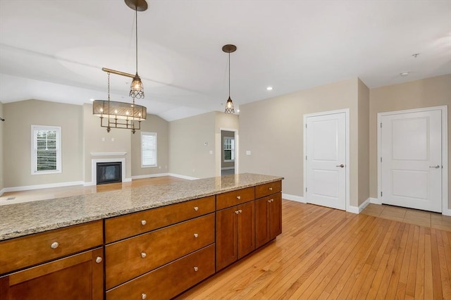 kitchen featuring light stone countertops, hanging light fixtures, vaulted ceiling, and light hardwood / wood-style floors