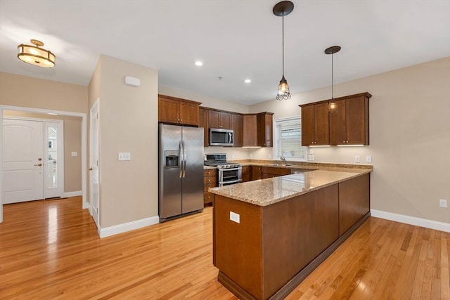 kitchen with kitchen peninsula, appliances with stainless steel finishes, light wood-type flooring, sink, and hanging light fixtures