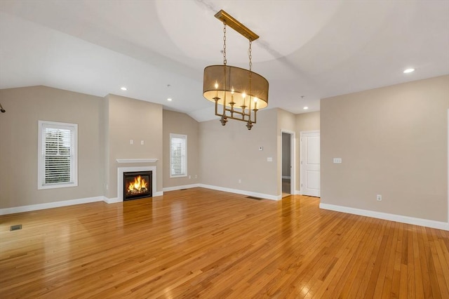 unfurnished living room with a notable chandelier, light wood-type flooring, a wealth of natural light, and vaulted ceiling