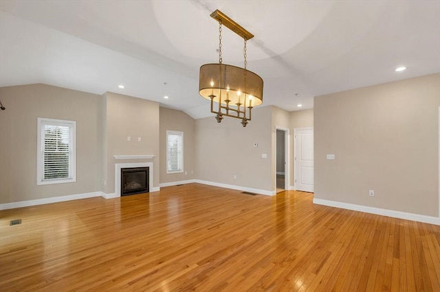 unfurnished living room with a healthy amount of sunlight, light hardwood / wood-style floors, lofted ceiling, and a notable chandelier