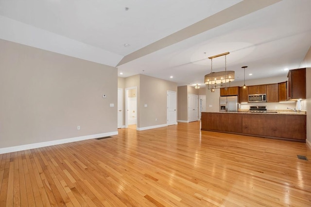 kitchen with kitchen peninsula, light hardwood / wood-style floors, pendant lighting, and appliances with stainless steel finishes