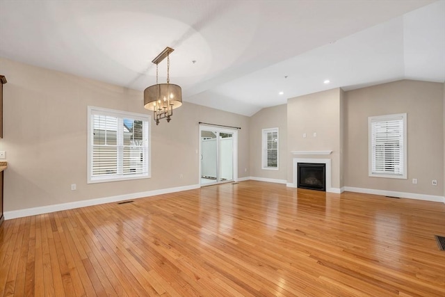 unfurnished living room featuring light hardwood / wood-style floors, lofted ceiling, and a notable chandelier