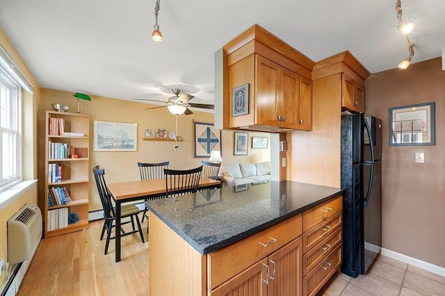 kitchen with black refrigerator, ceiling fan, an AC wall unit, a baseboard heating unit, and dark stone counters