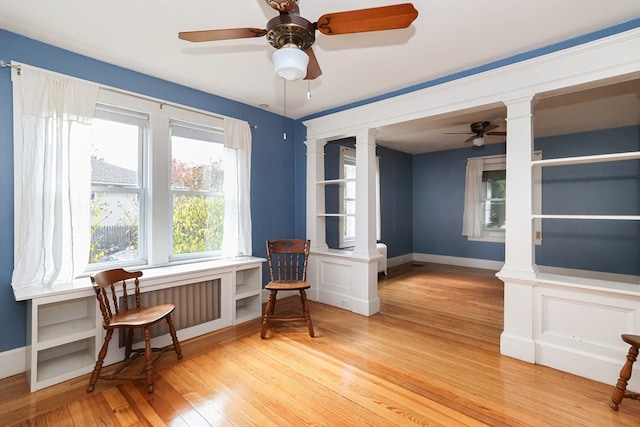 living area featuring ornate columns, ceiling fan, radiator heating unit, and wood-type flooring