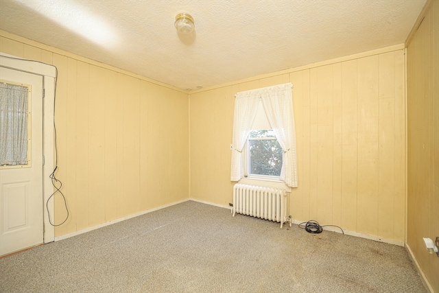 carpeted spare room with wooden walls, radiator heating unit, and a textured ceiling