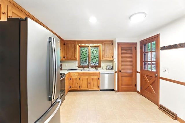 kitchen with stainless steel appliances, a sink, light countertops, light flooring, and brown cabinets
