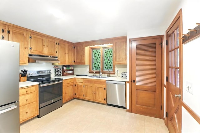 kitchen featuring appliances with stainless steel finishes, under cabinet range hood, a sink, light countertops, and light flooring