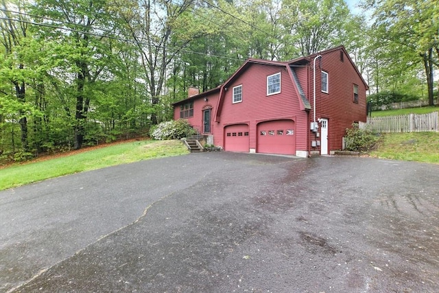 view of home's exterior featuring asphalt driveway, an attached garage, a chimney, fence, and a gambrel roof