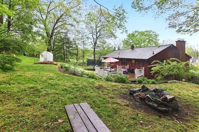 view of yard with a trampoline, a wooden deck, and an outbuilding