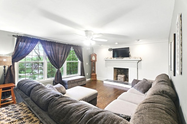 living area featuring a ceiling fan, crown molding, a brick fireplace, wood finished floors, and baseboards