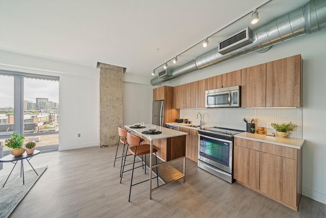 kitchen with sink, stainless steel appliances, backsplash, a breakfast bar, and light wood-type flooring