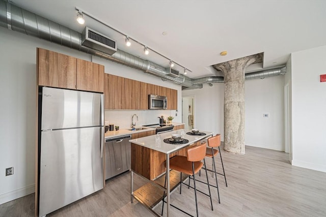 kitchen featuring appliances with stainless steel finishes, a kitchen breakfast bar, ornate columns, sink, and light hardwood / wood-style flooring