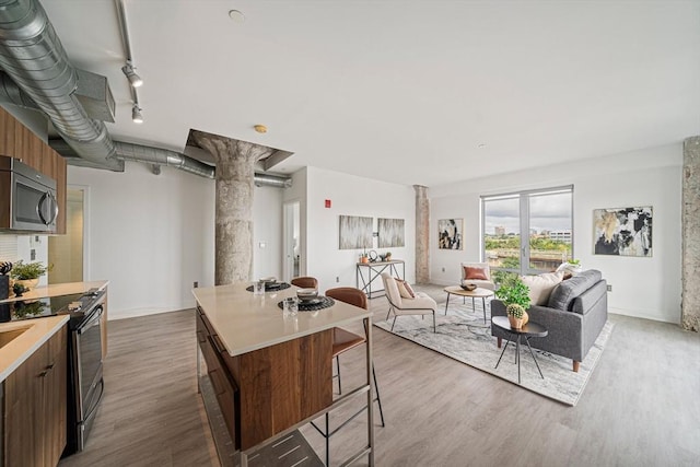 kitchen featuring a center island, track lighting, hardwood / wood-style flooring, stainless steel appliances, and decorative columns