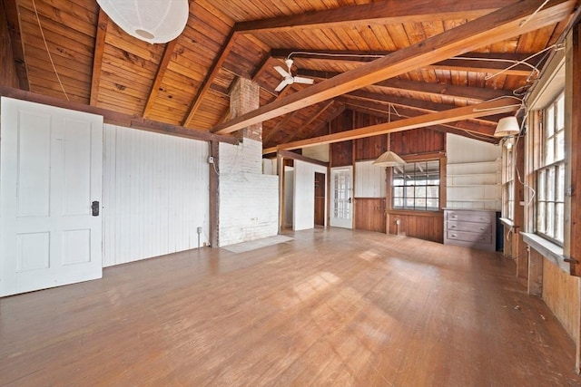 unfurnished living room featuring vaulted ceiling with beams, a ceiling fan, wood ceiling, wooden walls, and wood finished floors