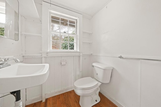 half bathroom with a wainscoted wall, toilet, and wood finished floors