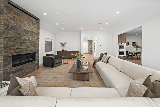 living room featuring a stone fireplace, wood finished floors, recessed lighting, and lofted ceiling