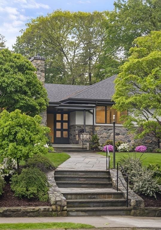 view of front facade with stone siding, a shingled roof, and a chimney
