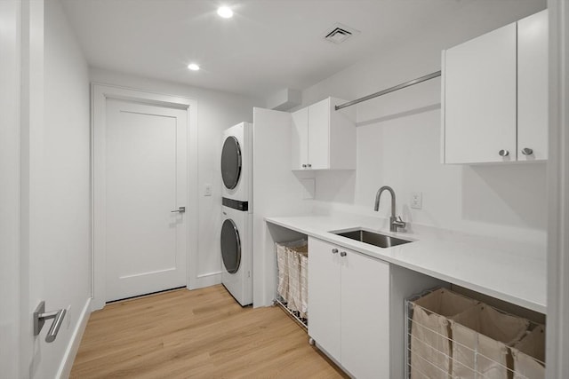 laundry area featuring stacked washer and clothes dryer, a sink, light wood finished floors, and recessed lighting