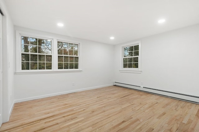 empty room featuring plenty of natural light, light hardwood / wood-style floors, and a baseboard heating unit