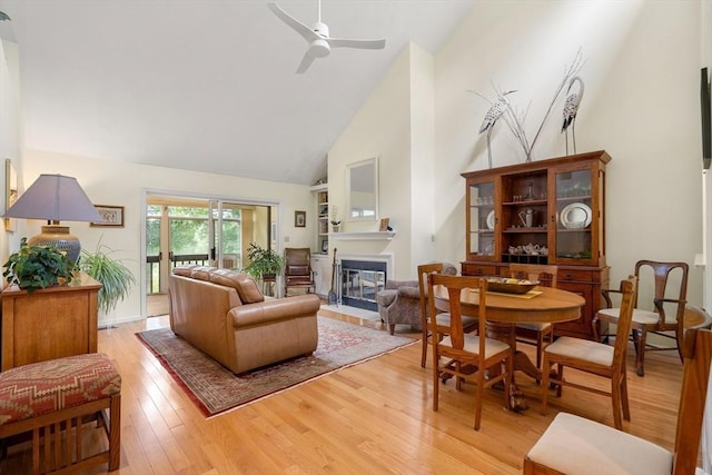 living area featuring high vaulted ceiling, a fireplace with flush hearth, light wood-style flooring, and a ceiling fan