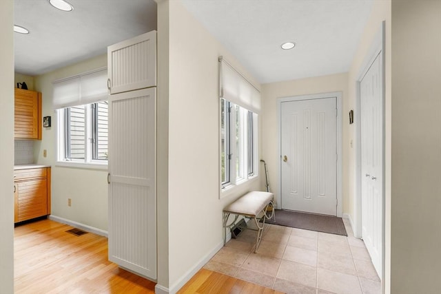 corridor featuring visible vents, light wood-style floors, a wealth of natural light, and baseboards