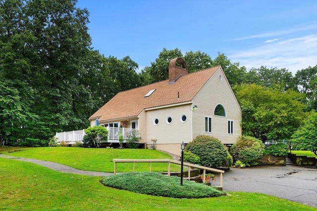 view of front of house with driveway, roof with shingles, a wooden deck, a chimney, and a front yard