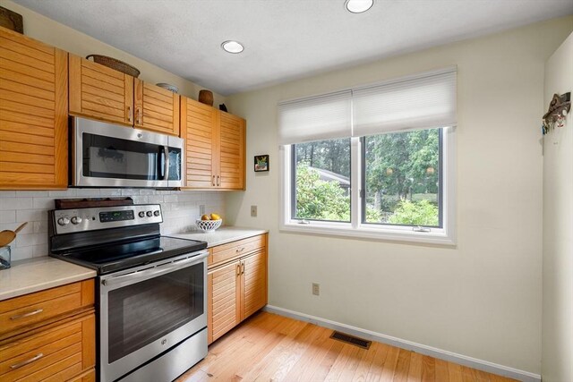 kitchen with backsplash, stainless steel appliances, and light hardwood / wood-style floors