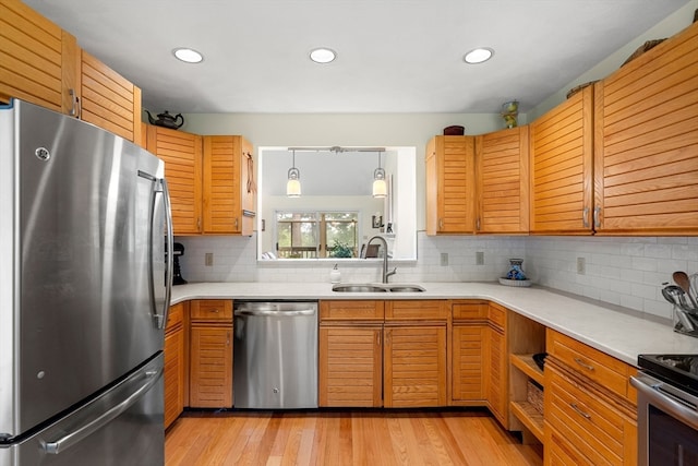 kitchen with pendant lighting, backsplash, appliances with stainless steel finishes, light hardwood / wood-style floors, and sink