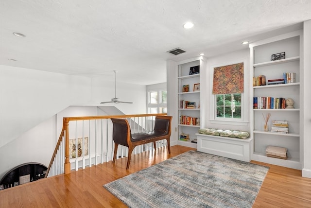 sitting room with a textured ceiling, built in features, hardwood / wood-style flooring, and ceiling fan