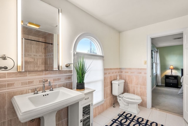 bathroom featuring toilet, tile walls, tile patterned flooring, and a tile shower