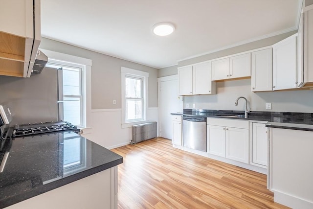 kitchen featuring radiator, light wood-style floors, white cabinets, a sink, and appliances with stainless steel finishes