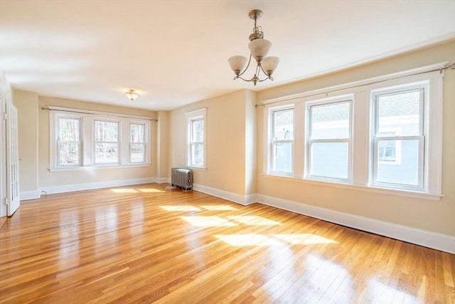 unfurnished room featuring baseboards, an inviting chandelier, radiator heating unit, and light wood-style floors