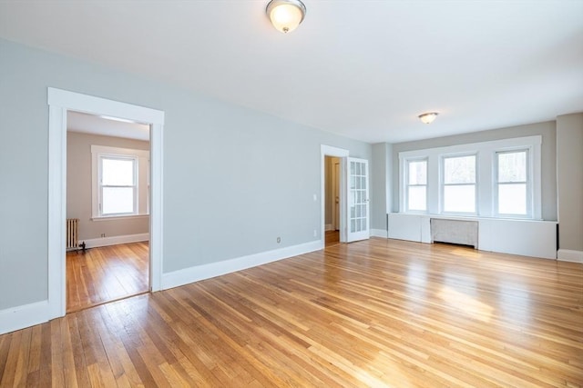 unfurnished living room with light wood-type flooring, baseboards, and radiator heating unit