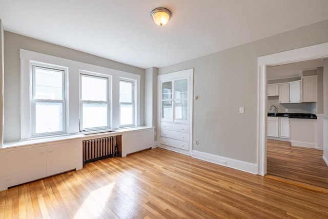 spare room with a sink, radiator, baseboards, and light wood-style flooring