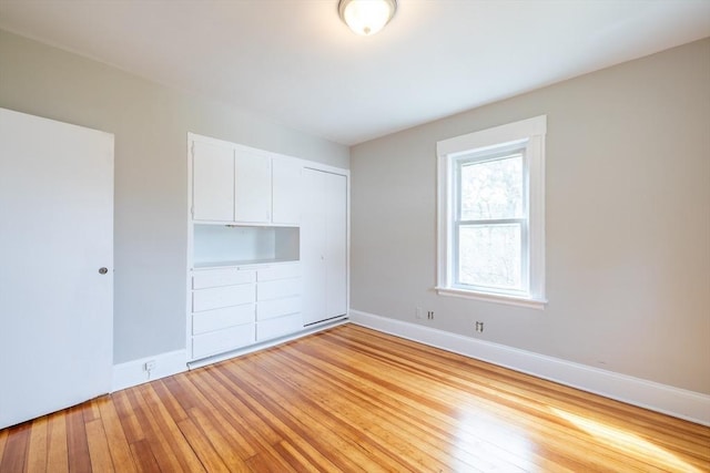 unfurnished bedroom with baseboards, light wood-style flooring, and a closet