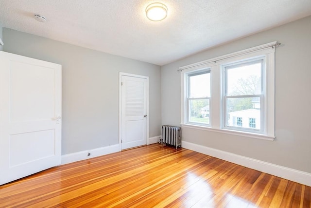 spare room featuring radiator heating unit, baseboards, and light wood finished floors