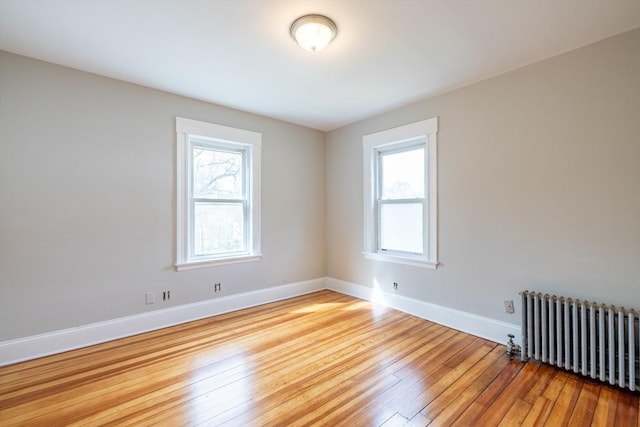 unfurnished room with radiator, baseboards, hardwood / wood-style flooring, and a wealth of natural light