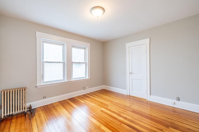 unfurnished room featuring baseboards, radiator, and light wood-style floors