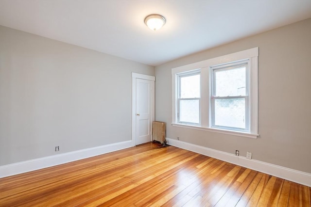 unfurnished room with baseboards, light wood finished floors, and radiator