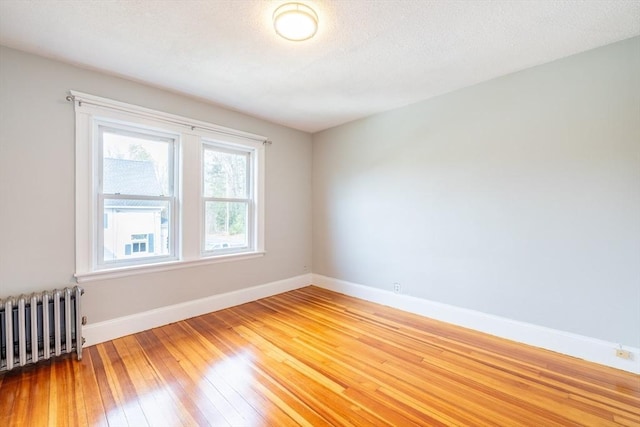 empty room featuring a textured ceiling, baseboards, radiator heating unit, and light wood-style floors