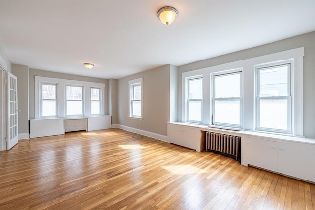 unfurnished living room featuring radiator heating unit, baseboards, and light wood-type flooring