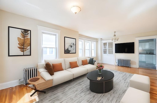 living room with wood finished floors, baseboards, radiator heating unit, and a notable chandelier