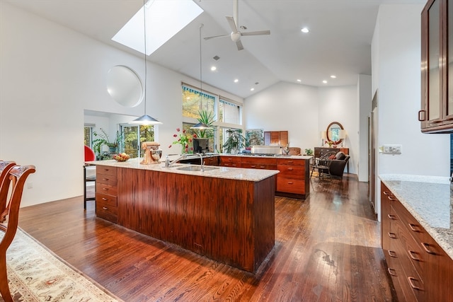 kitchen featuring hanging light fixtures, a large island with sink, high vaulted ceiling, dark wood-type flooring, and light stone counters