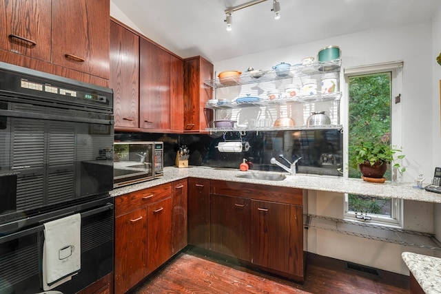 kitchen featuring tasteful backsplash, light stone countertops, black double oven, dark wood-type flooring, and sink