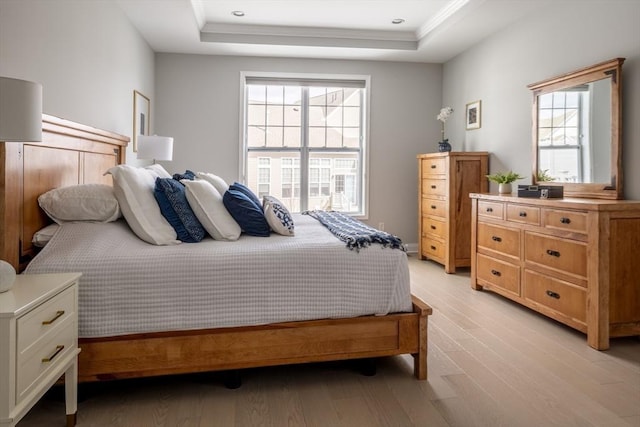 bedroom with ornamental molding, a tray ceiling, and light wood-type flooring