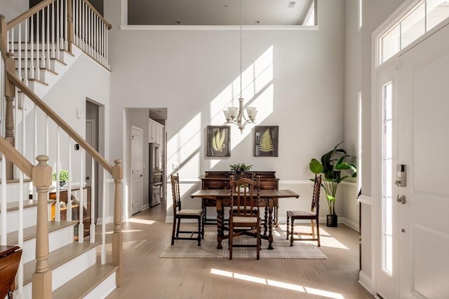 dining space with stairs, light wood finished floors, a high ceiling, and a notable chandelier