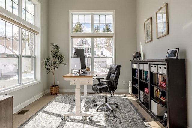 home office featuring a wealth of natural light, visible vents, baseboards, and wood finished floors