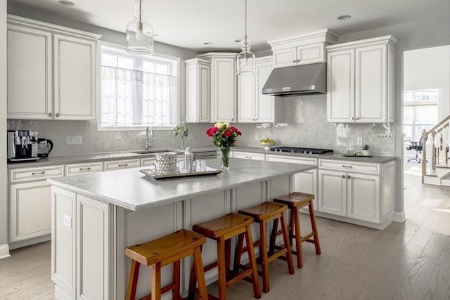 kitchen with a center island, a sink, gas cooktop, under cabinet range hood, and a kitchen bar