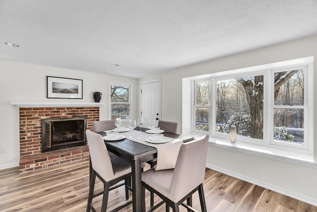 dining area featuring a brick fireplace, hardwood / wood-style floors, a textured ceiling, and a healthy amount of sunlight